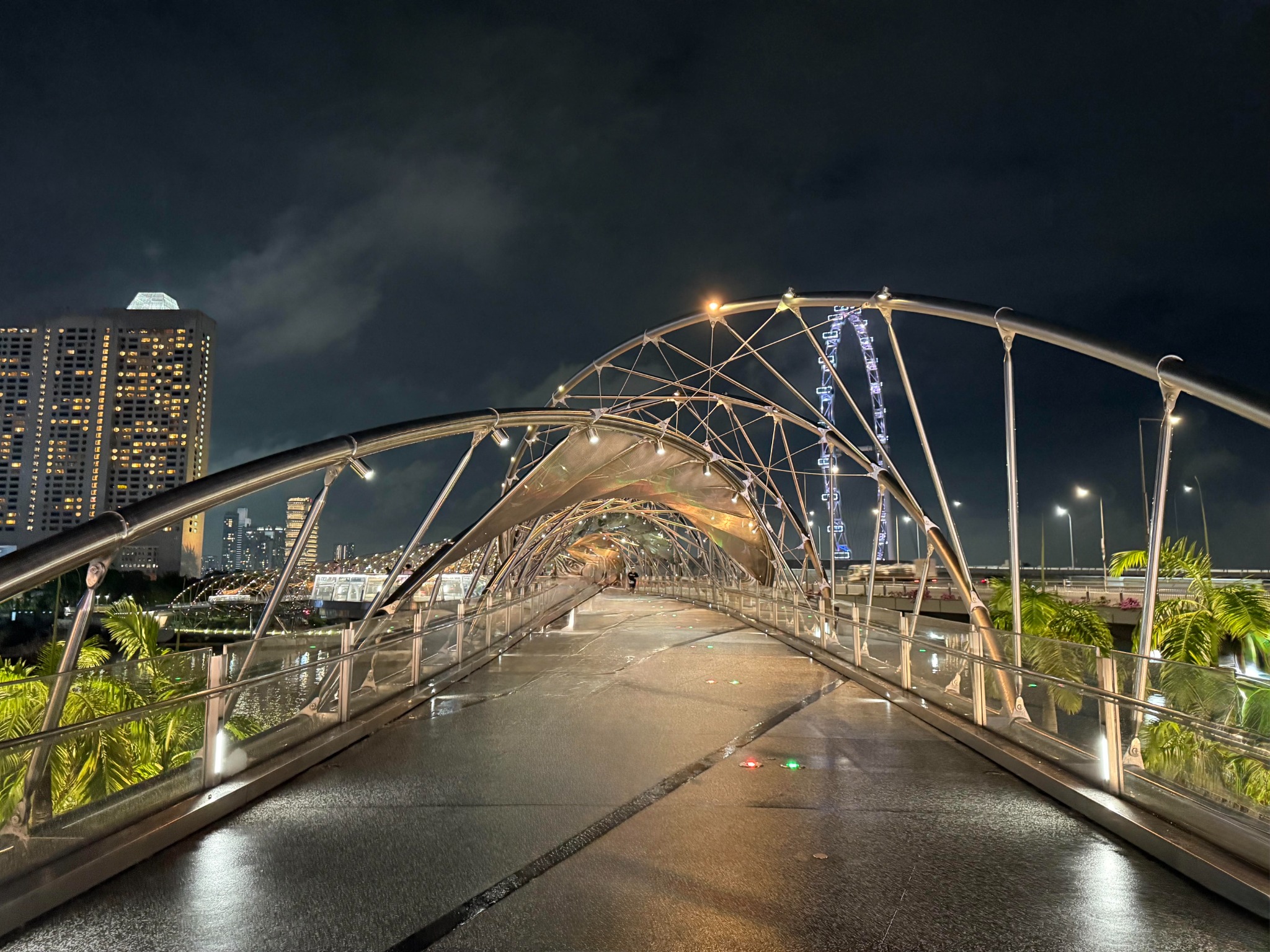 An illuminated pedestrian bridge at night, its intersecting curves leading forward through the city.