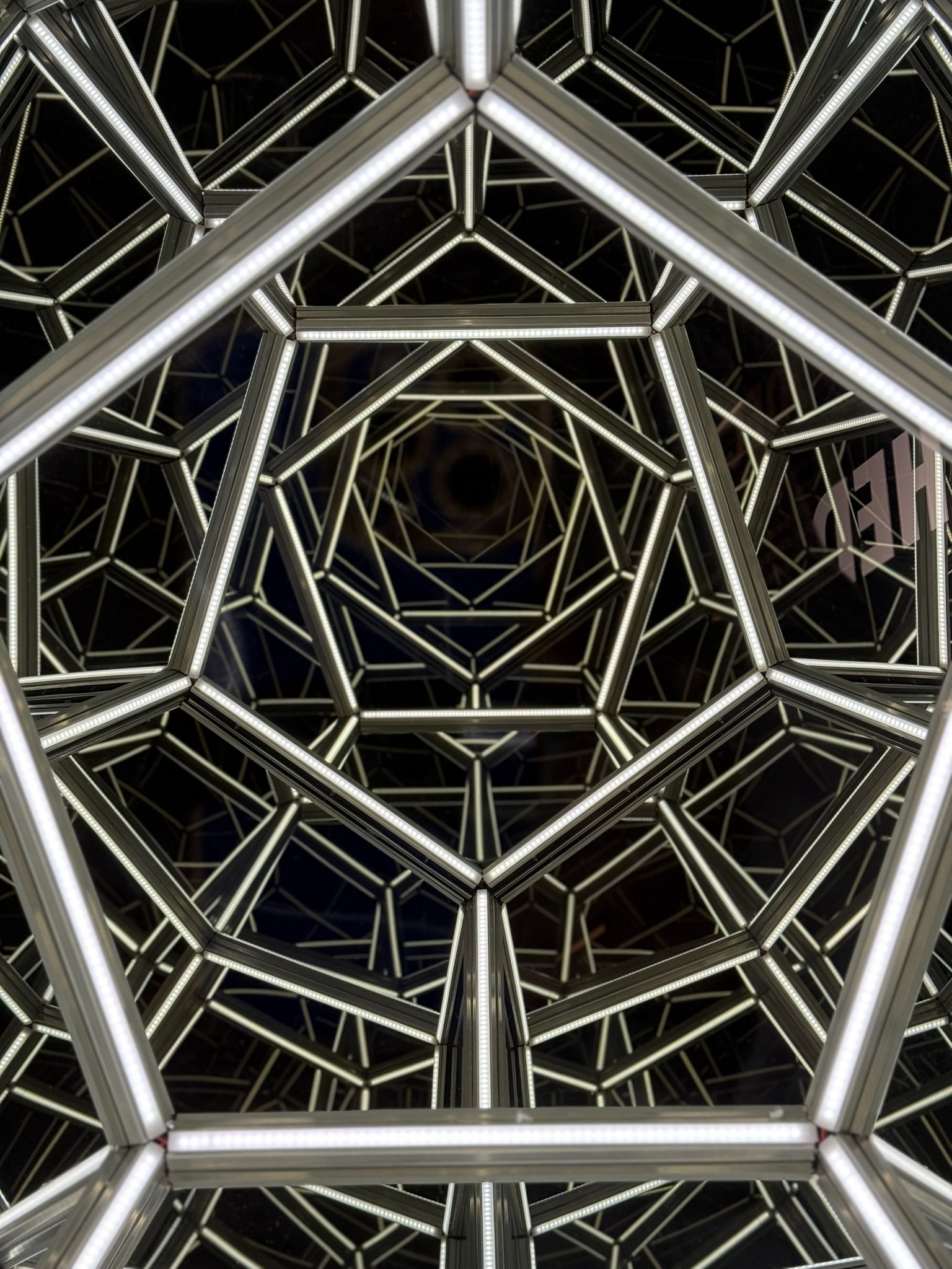 A mirrored geometric installation forming a luminous tunnel of repeated shapes.