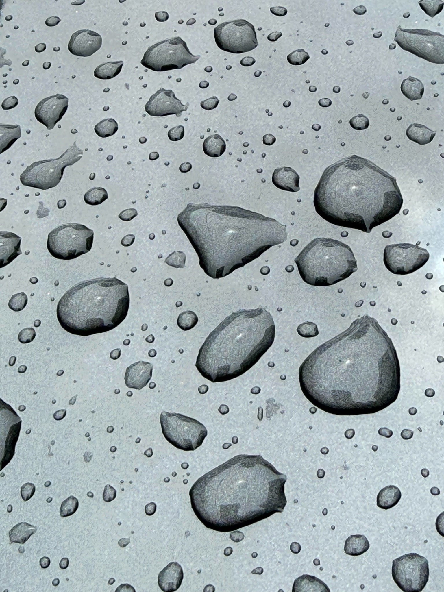 Raindrops of different sizes clinging to the vertical silver panel of a car.