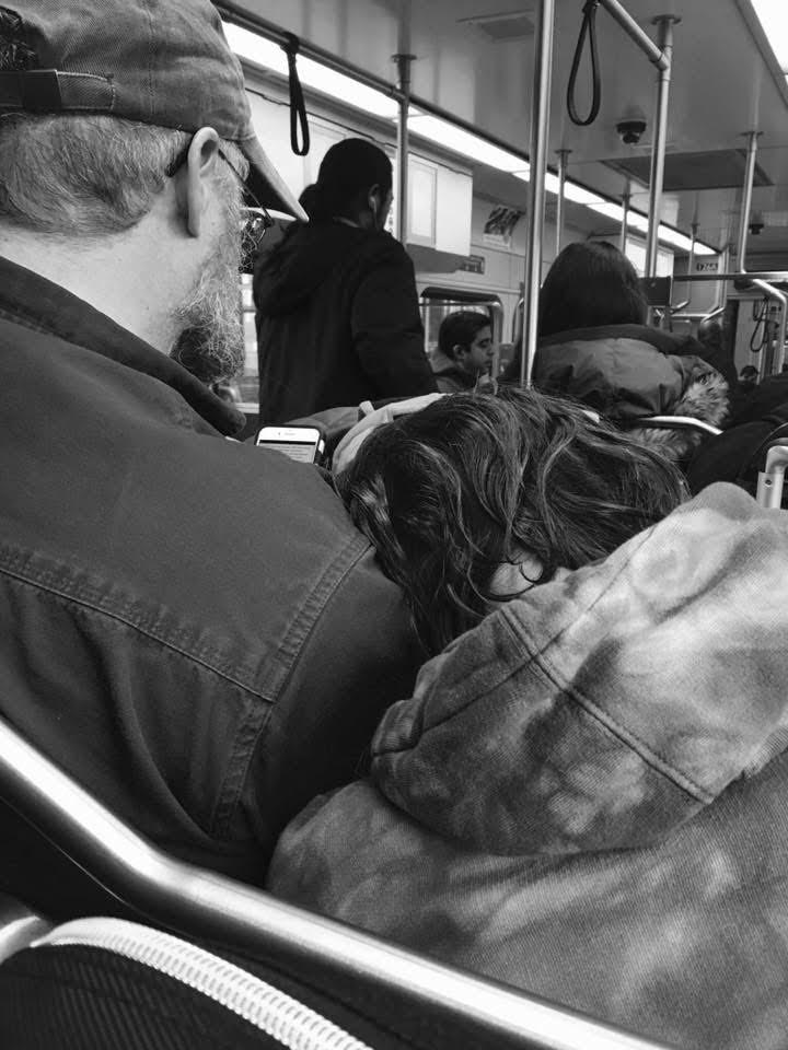 A child resting her head against her father on a crowded train at the end of the day.